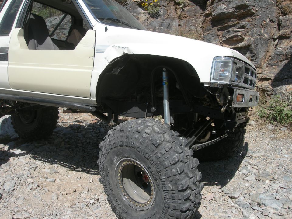 White Toyota pickup with large off-road tires and suspension, parked on rocky terrain
