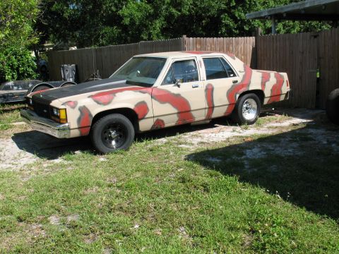 1985 Ford Crown Victoria LTD - This sedan features a distinctive tan and red camouflage paint scheme, parked outdoors.