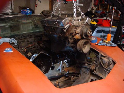 1975 Chevrolet Corvette - Engine being lowered into the engine bay of an orange car with the hood open.