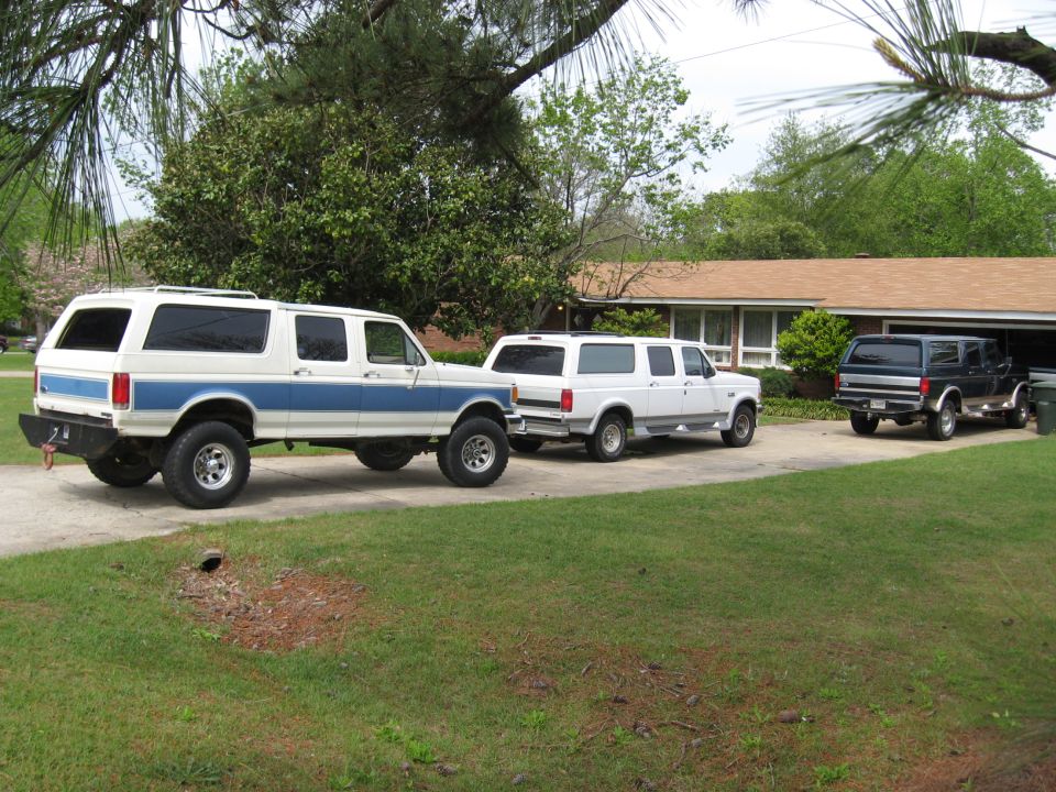Three extended four-door Ford Bronco conversions parked in a row on a driveway, rear view