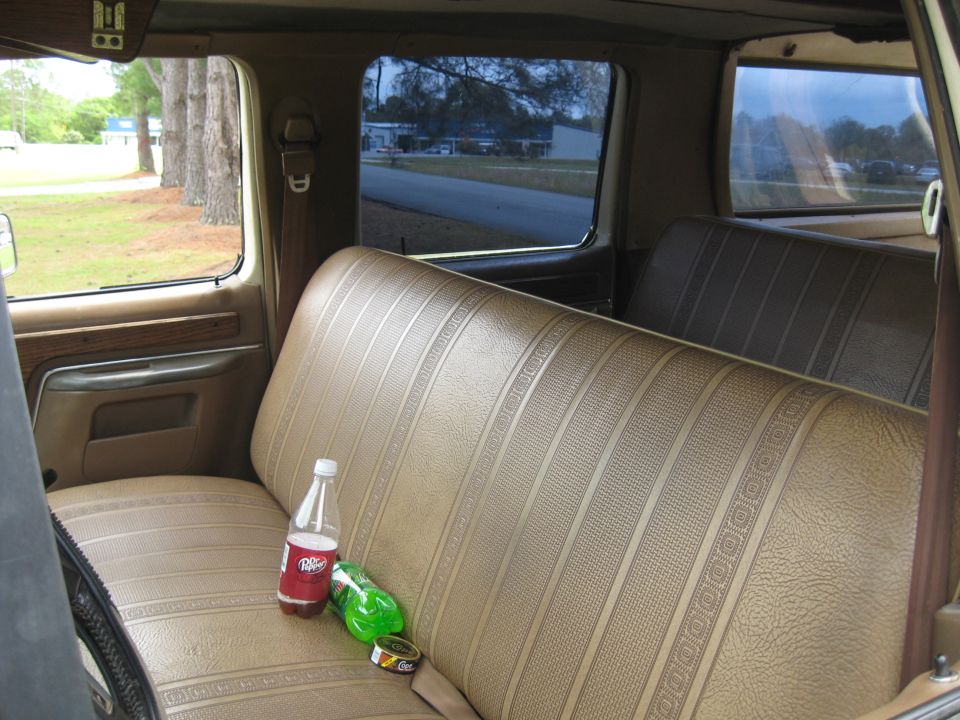 Tan patterned bench seat inside a vehicle with two drink bottles and a can on it