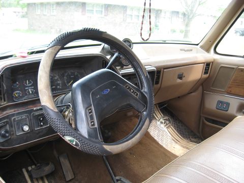 1995 Ford C-350 (Centurion Conversions) - The interior of a truck shows a tan dashboard, Ford steering wheel, and patterned seat fabric.