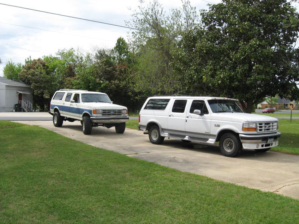 White and blue-and-white extended four-door Ford Bronco conversions parked on a driveway