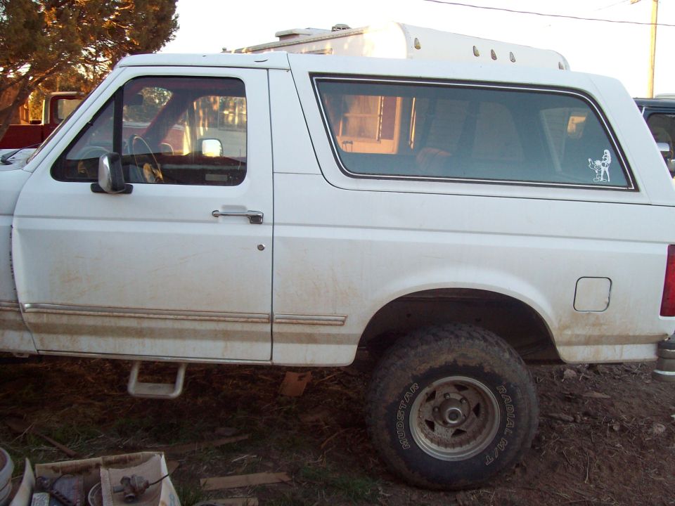 Rear side view of a white Ford Bronco in a dirt yard