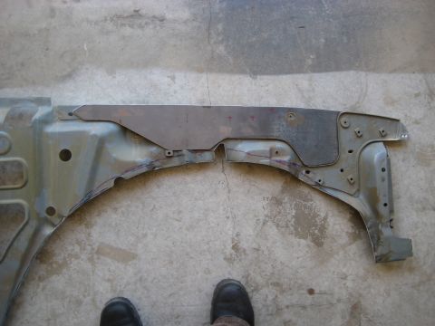 1996 Ford Bronco - Sheet-metal repair panel laid over a truck's inner fender apron on a concrete shop floor, with a freshly cut patch piece marked in red cray…