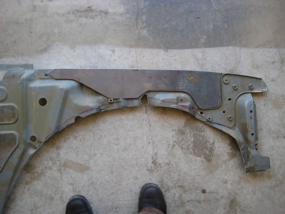 Cut sheet-metal patch panel laid over a truck inner fender apron on a shop floor