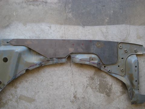 1996 Ford Bronco - A stripped bare-metal front fender panel laid face-up on a concrete floor during rust repair. A large patch of the upper section has been s…