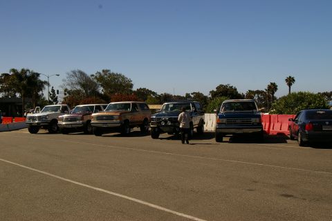 1986 Ford Bronco - Multiple Ford Broncos and trucks are parked in a line under a clear blue sky.