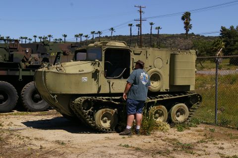 1986 Ford Bronco - A person stands beside an olive green tracked vehicle, with other military vehicles in the background.