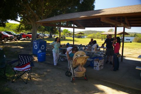 1986 Ford Bronco - A group enjoys a picnic at a park with a lake and hills in the background, while vehicles are parked nearby.