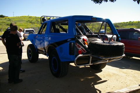 1986 Ford Bronco - A modified blue Ford Bronco is parked outdoors with people nearby and another vehicle to its right.