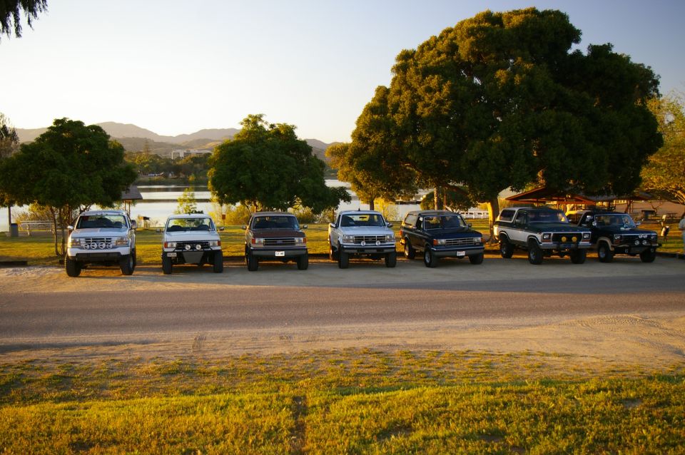 1986 Ford Bronco and other SUVs parked in a row by a lake