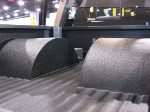 1980 Ford Bronco - The interior of a truck bed shows two black textured wheel wells and a ribbed floor.