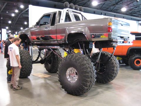 1980 Ford Bronco - A heavily modified pickup truck with oversized tires and a lifted suspension is displayed indoors.