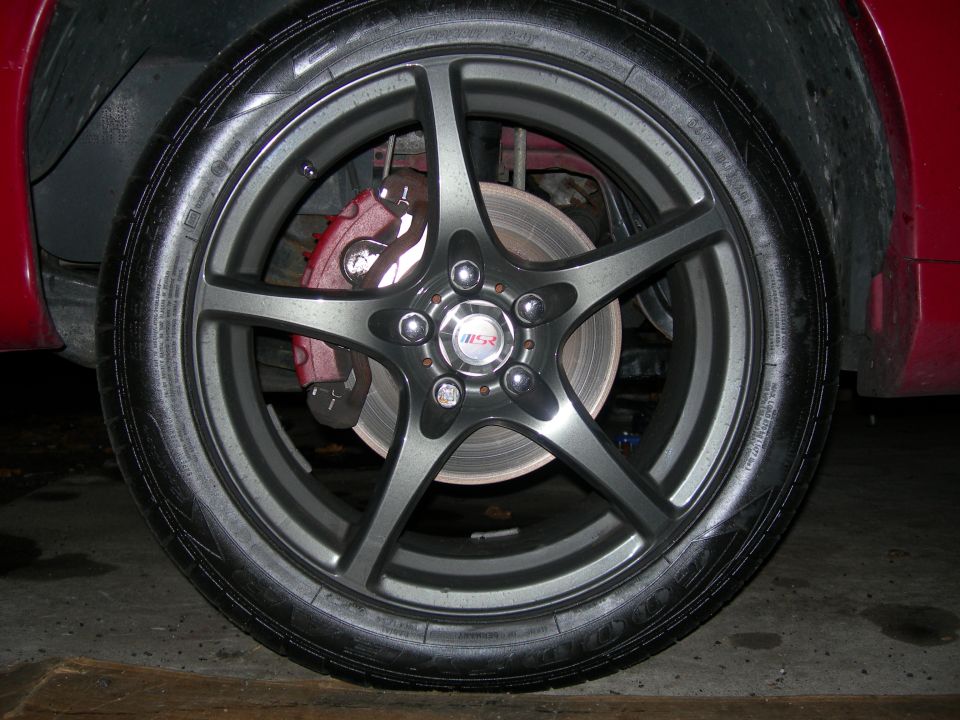 Gunmetal five-spoke alloy wheel with red brake caliper on a red car
