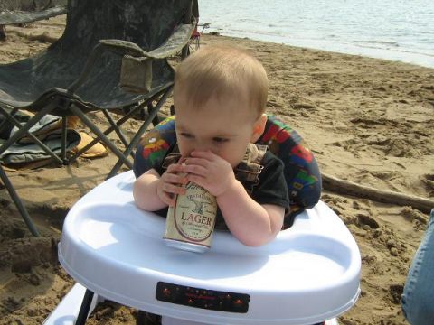 1990 Ford Bronco - A baby sits in a walker on a sandy beach, holding a can of lager near their mouth.