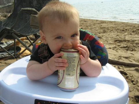 1990 Ford Bronco - A baby sits in a high chair on the sand, curiously examining a beverage can.