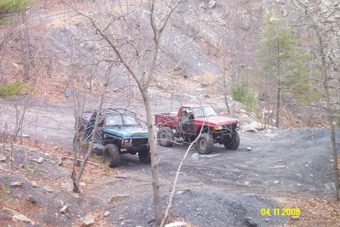 1992 Ford Bronco - Modified off-road vehicles are parked on a dirt path in a rocky, wooded area.