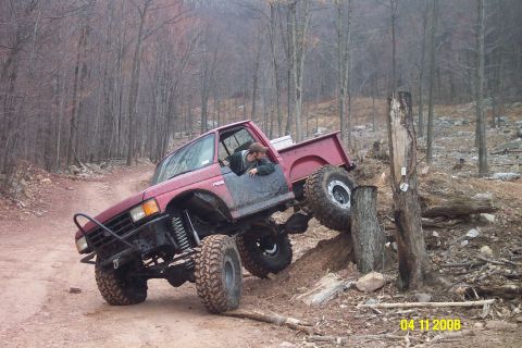 1992 Ford Bronco - A red pickup truck navigates a challenging off-road course with a driver visible.