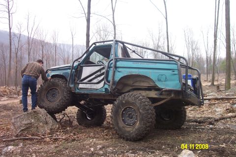 1992 Ford Bronco - Modified SUV with extensive roll cage and off-road tires navigating rocky terrain.