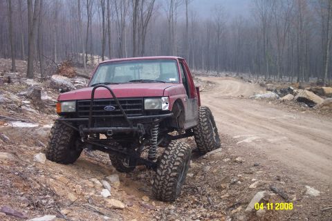 1992 Ford Bronco - This modified Ford truck navigates a rough, unpaved trail through a forest.