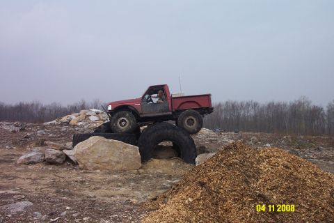 1992 Ford Bronco - A red pickup truck navigates an off-road course with large tires and obstacles.