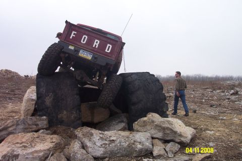1992 Ford Bronco - A red pickup truck navigates a rocky obstacle course, its large tires gripping the terrain.