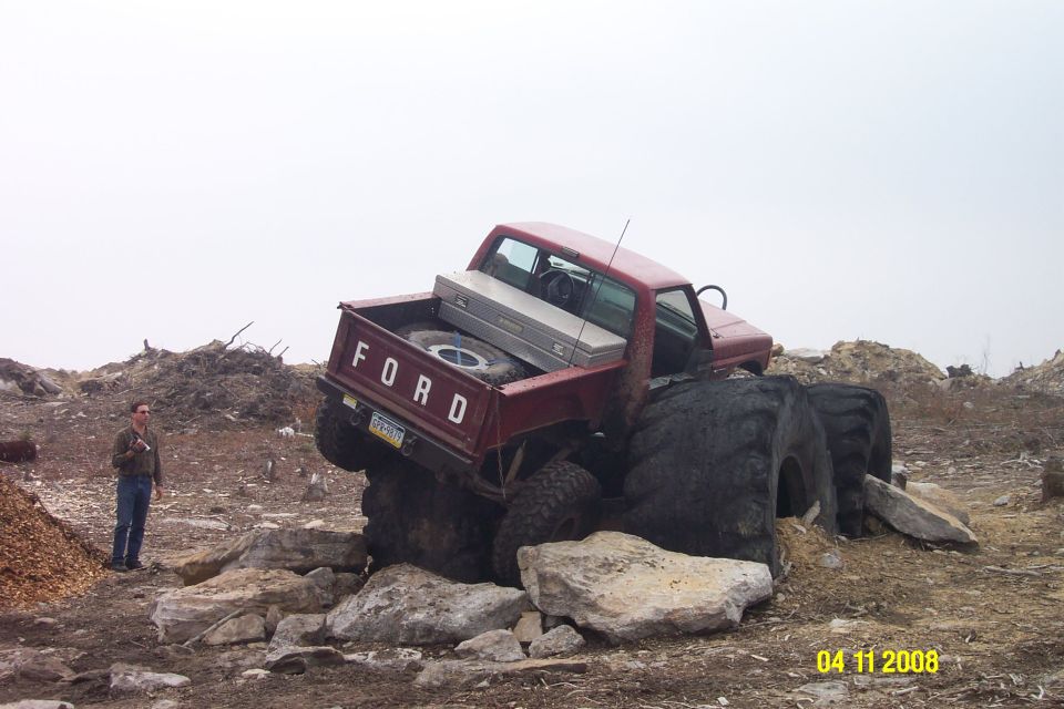 red Ford pickup truck with huge tires stuck on rocks, guy standing nearby