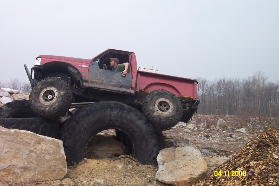 Red pickup truck with large tires on rocks and tires
