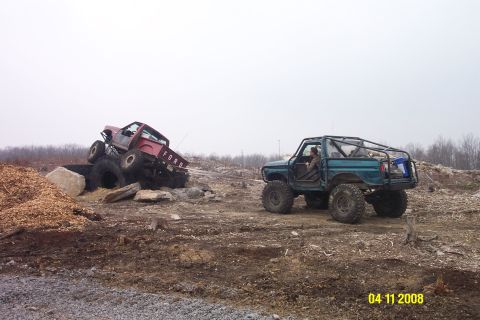 1992 Ford Bronco - Two modified trucks navigating a challenging off-road course with obstacles.