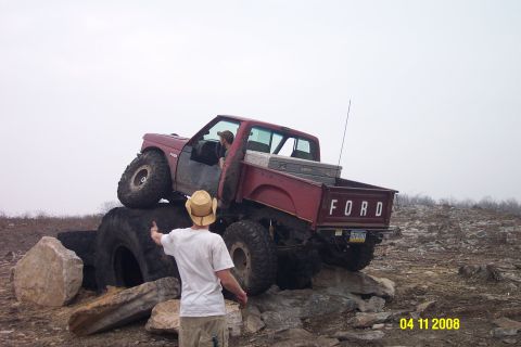 1992 Ford Bronco - This red Ford pickup truck is off-roading over large rocks and tires. The year appears to be 1992.