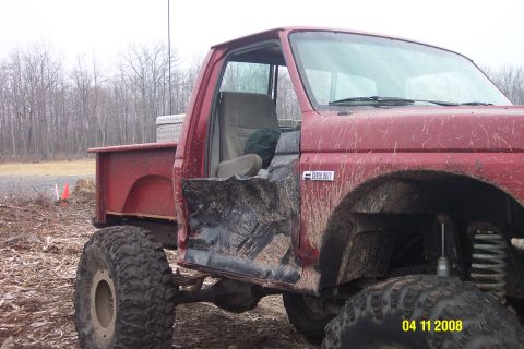 1992 Ford Bronco - A red pickup truck sits in a muddy, wooded area with significant damage to its driver's side door.