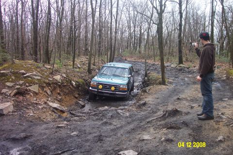 1992 Ford Bronco - A green SUV navigates a challenging muddy path through a dense forest.