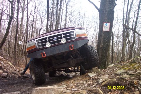 1992 Ford Bronco - A maroon 1992 Ford Bronco navigates a challenging rocky trail, its off-road capabilities.