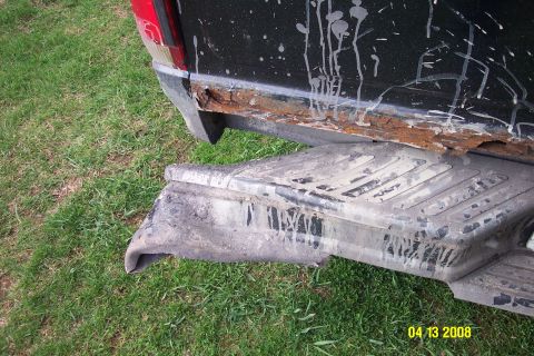 1992 Ford Bronco - The rear fender and bumper of a black pickup truck show extensive rust damage.