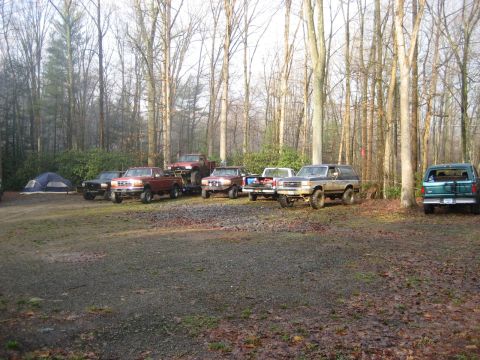1991 Ford Bronco - Multiple Ford trucks and a Bronco gathered in a wooded campsite.