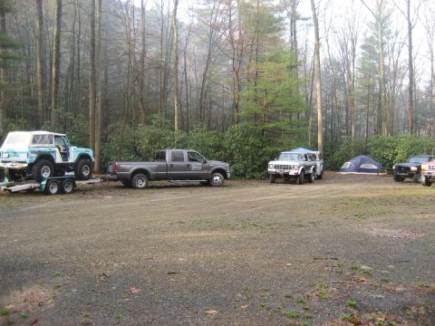 1991 Ford Bronco - A group of off-road vehicles and camping gear are gathered in a forest clearing.