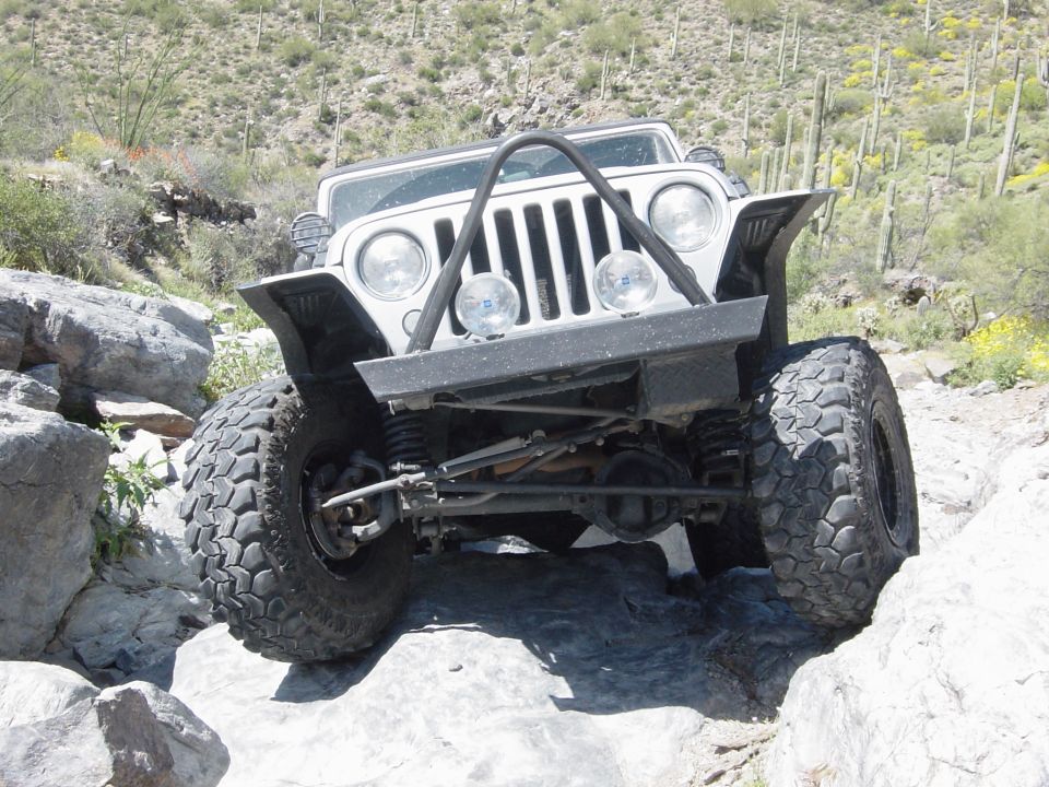 Front view of a silver Jeep Wrangler on a rocky trail, with large tires and a custom bumper