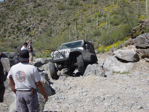2004 Jeep Wrangler - A silver Jeep Wrangler tackles a challenging rocky trail in a desert landscape.