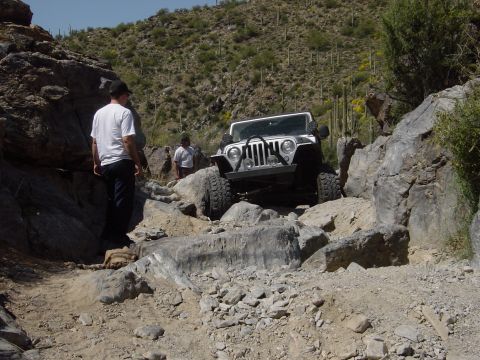 2004 Jeep Wrangler - A white 2004 Jeep Wrangler tackles a challenging rocky path in a desert environment.