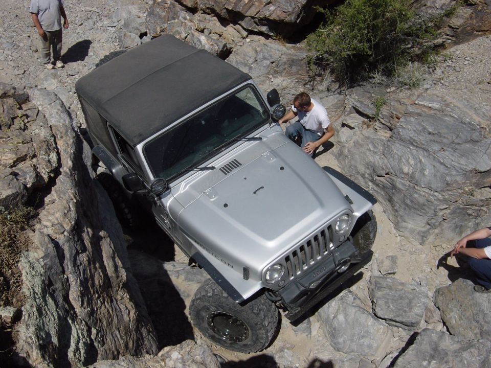 Silver 2004 Jeep Wrangler TJ Rubicon navigating a rocky trail, with people observing