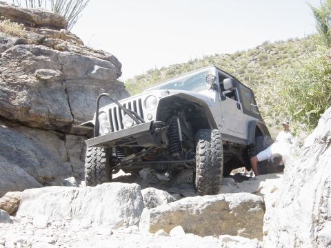 2004 Jeep Wrangler - A Jeep Wrangler is shown off-roading on a rocky trail with two individuals observing.
