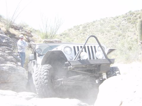 2004 Jeep Wrangler - A 2004 Jeep Wrangler navigates a dusty, rocky off-road path with a person standing nearby.
