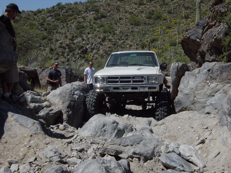 White Toyota pickup truck navigating a rocky trail with people watching