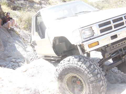 2004 Jeep Wrangler - A modified white pickup truck tackles a challenging rocky trail, with a person watching from the side.