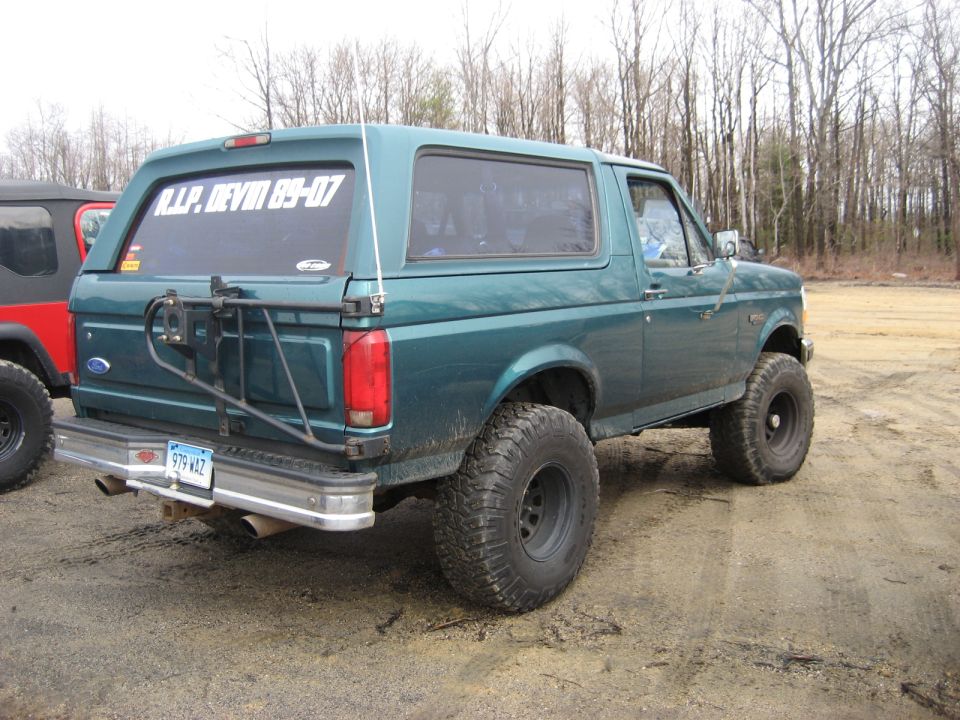 Green 1991 Ford Bronco with off-road tires and a rear-mounted spare tire carrier. Another vehicle is partially visible to the left