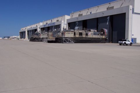 1990 Ford Bronco - A white pickup truck is parked on an airfield in front of hangars housing hovercraft.