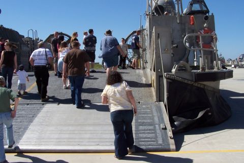 1990 Ford Bronco - A group of people are seen boarding a large military landing craft, with a clear blue sky overhead.