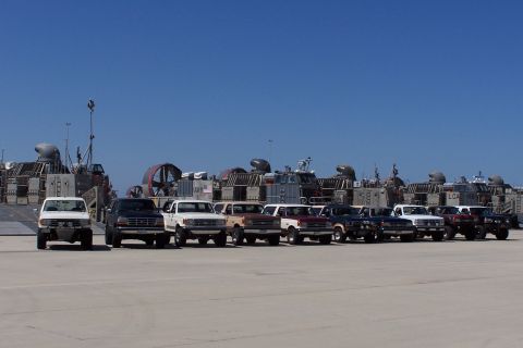 1990 Ford Bronco - A row of Ford trucks and SUVs from the early 1990s are parked on a tarmac with hovercraft in the background.