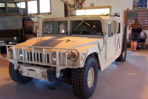 1990 Ford Bronco - A tan Humvee is displayed indoors, with a poster of a Marine in the background.